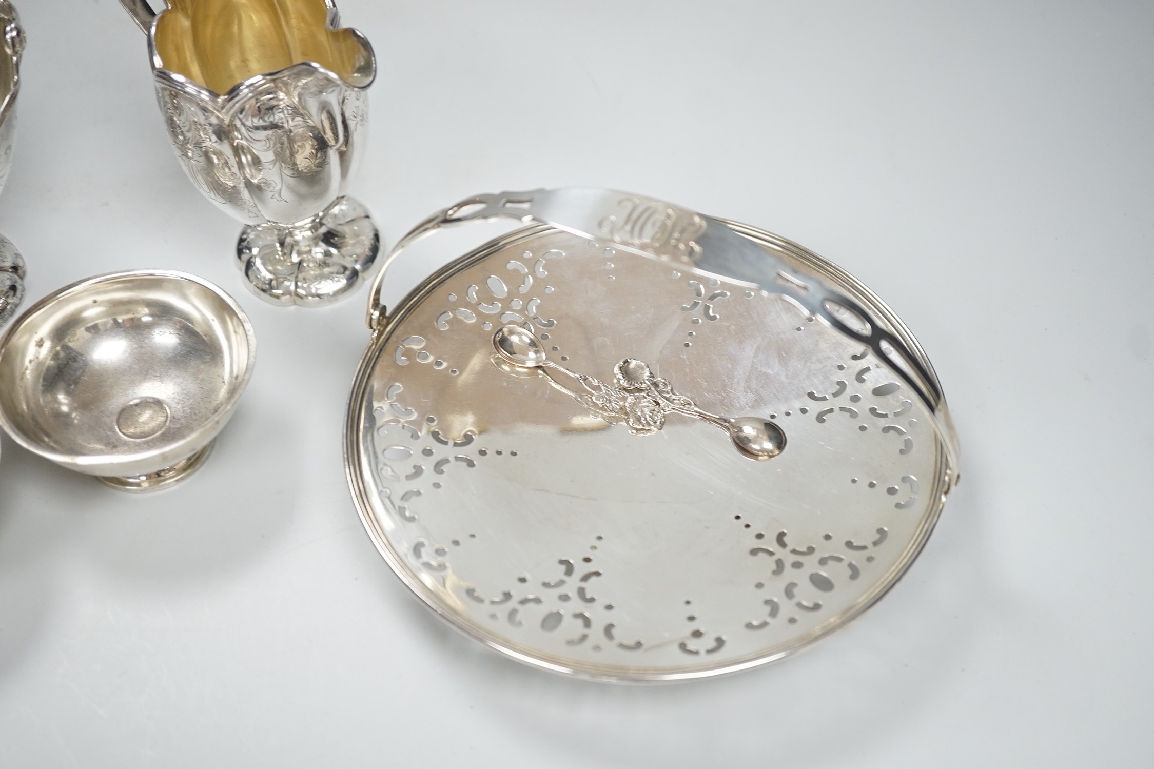 A sterling sugar basket, diameter 9.9cm, a sterling shallow basket dish, sterling cream jug and pair of sterling salts with spoons, 20.6oz.